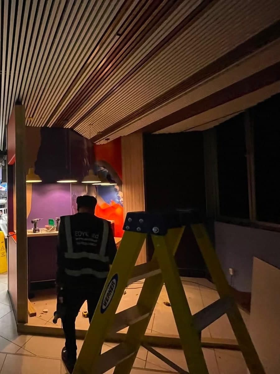 EDYK team member working at a new counter and partition under a slatted timber ceiling, with a ladder in the foreground