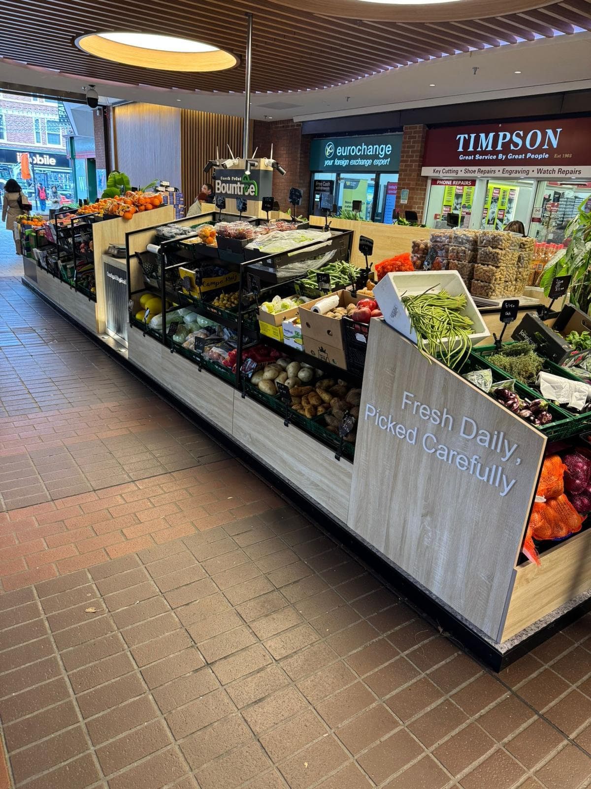 Retail island unit in a shopping centre with tiered shelving and a timber panel